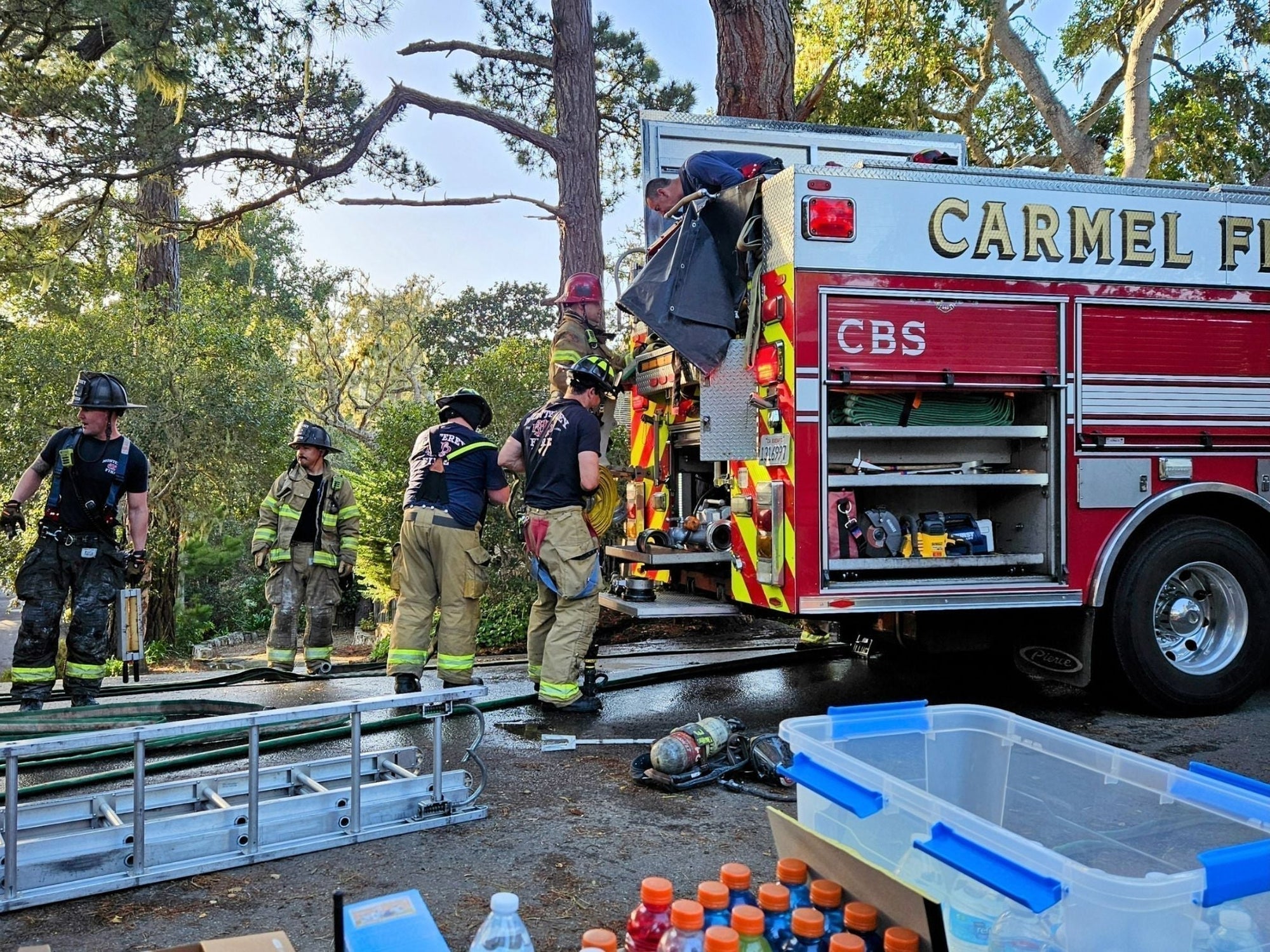 Carmel Fire Department firefighters stand beside a table filled with emergency supplies provided by Carmel CERT, highlighting community preparedness efforts.